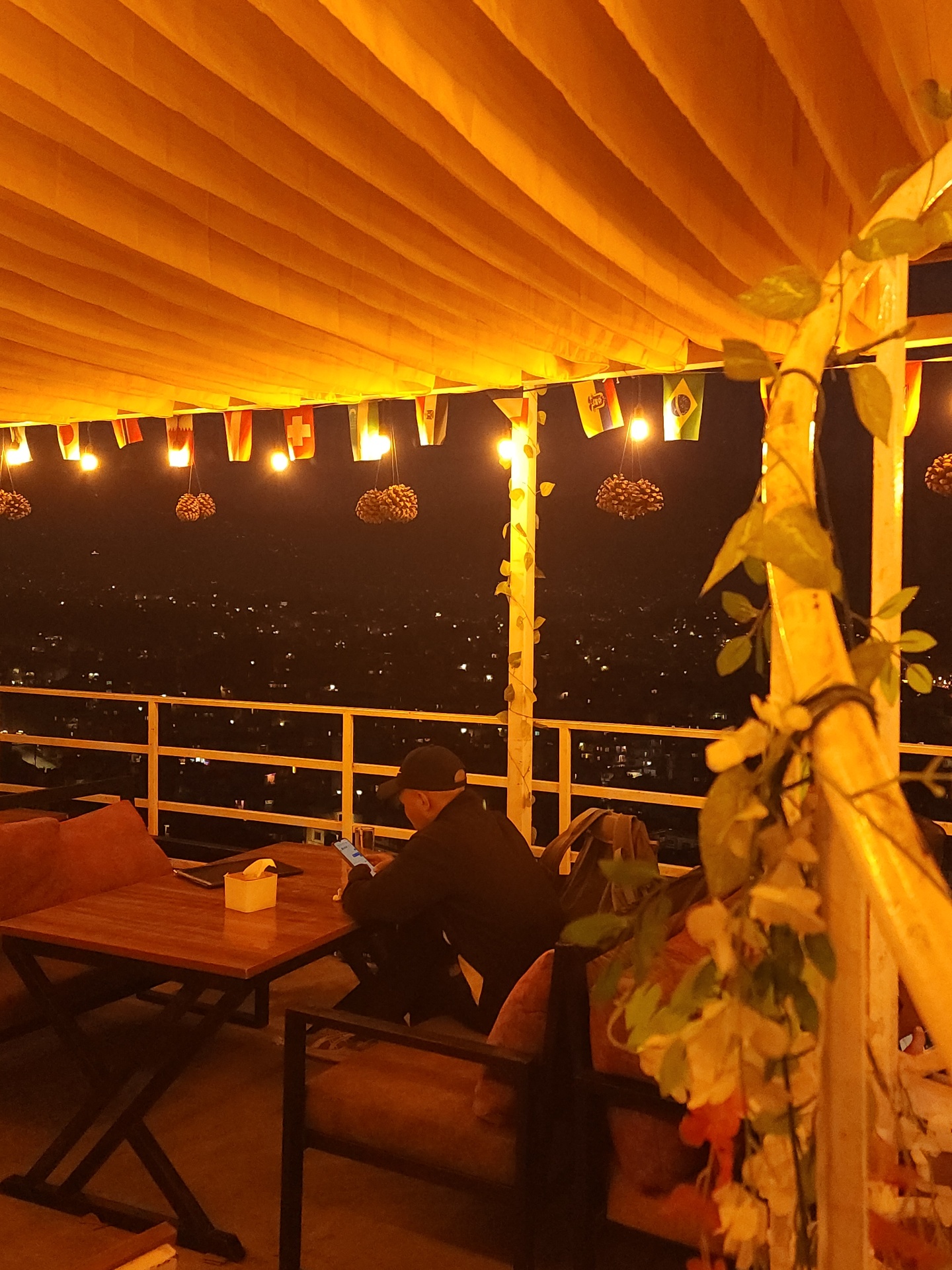 Evening corner table under warm festoon lights with vines and the city glowing below
