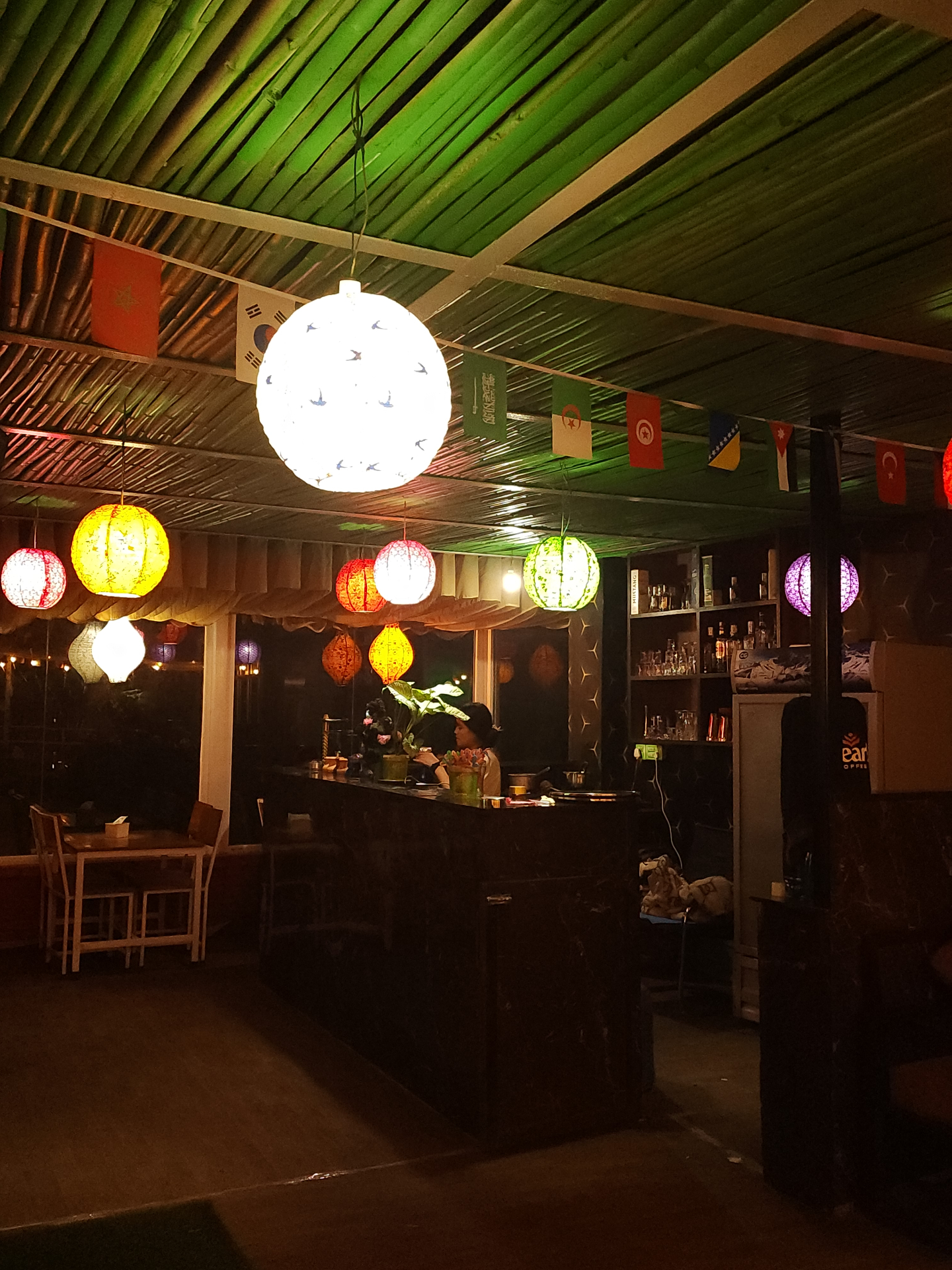 The bar counter at Ask Restaurant & Bar lit by colourful paper lanterns under a bamboo ceiling
