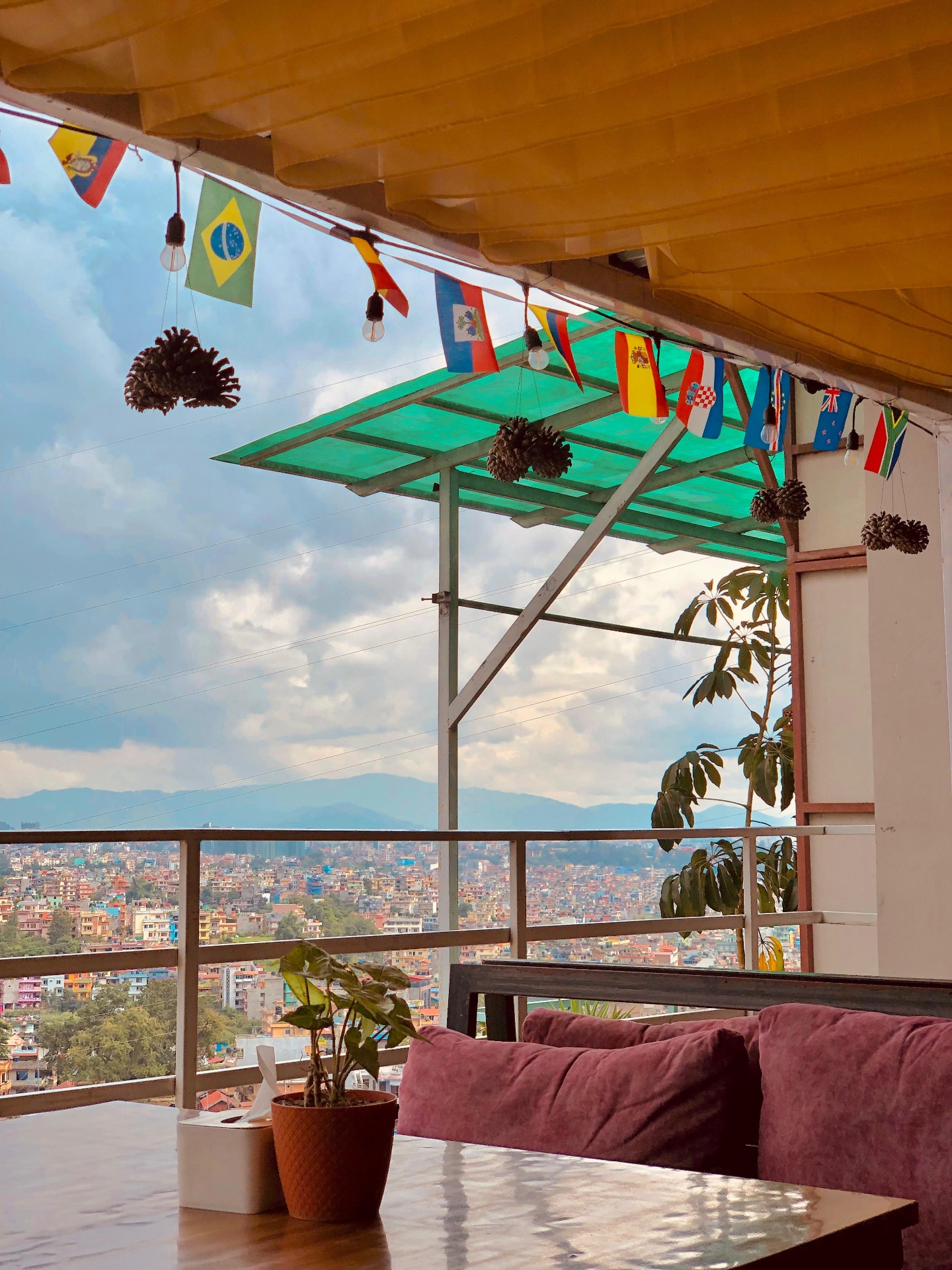 Daytime rooftop seating at Ask Restro & Bar with pink sofas, hanging flags and a view over the Kathmandu valley