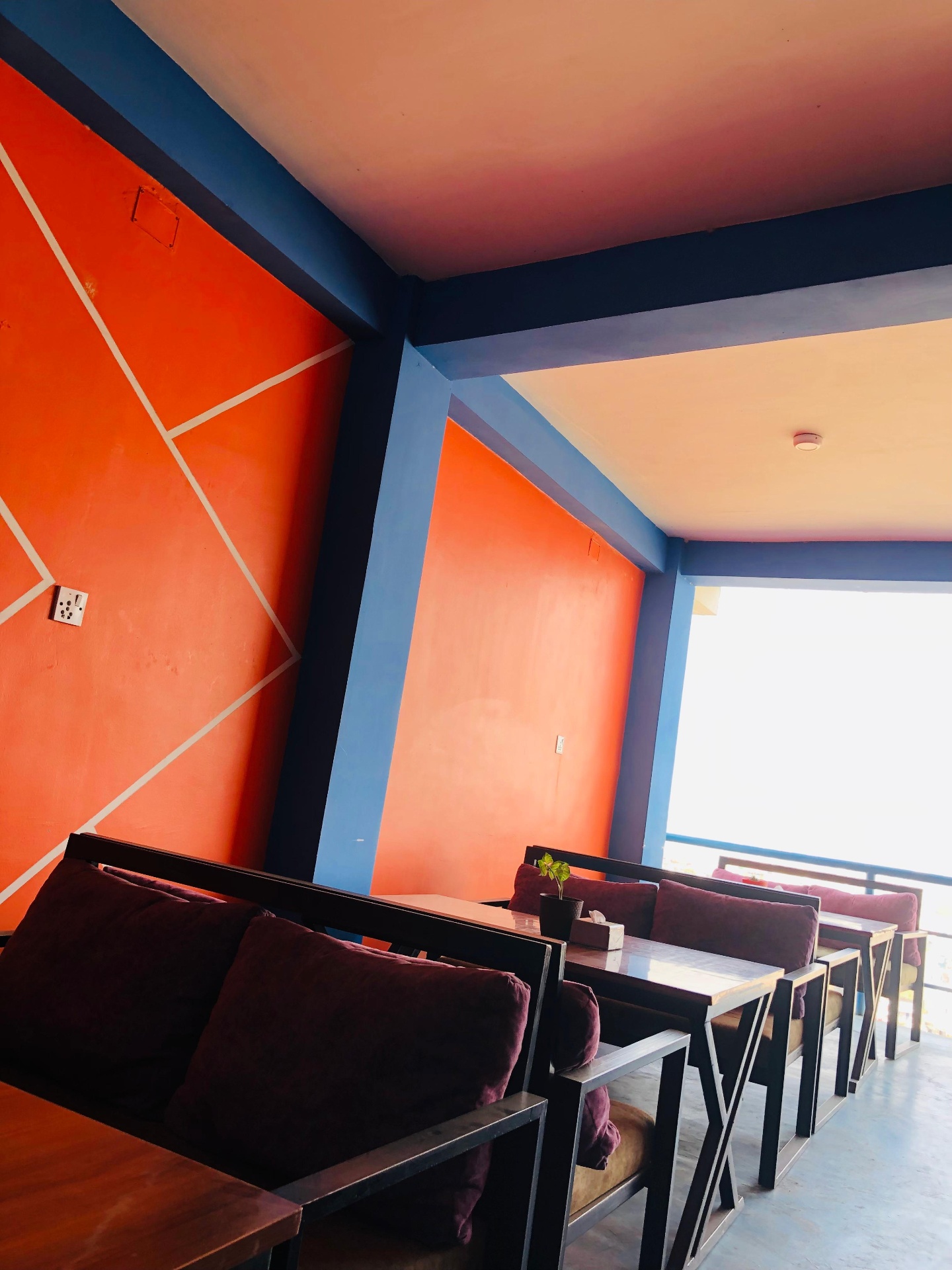 Indoor booth seating with orange geometric walls, blue beams and plum velvet sofas