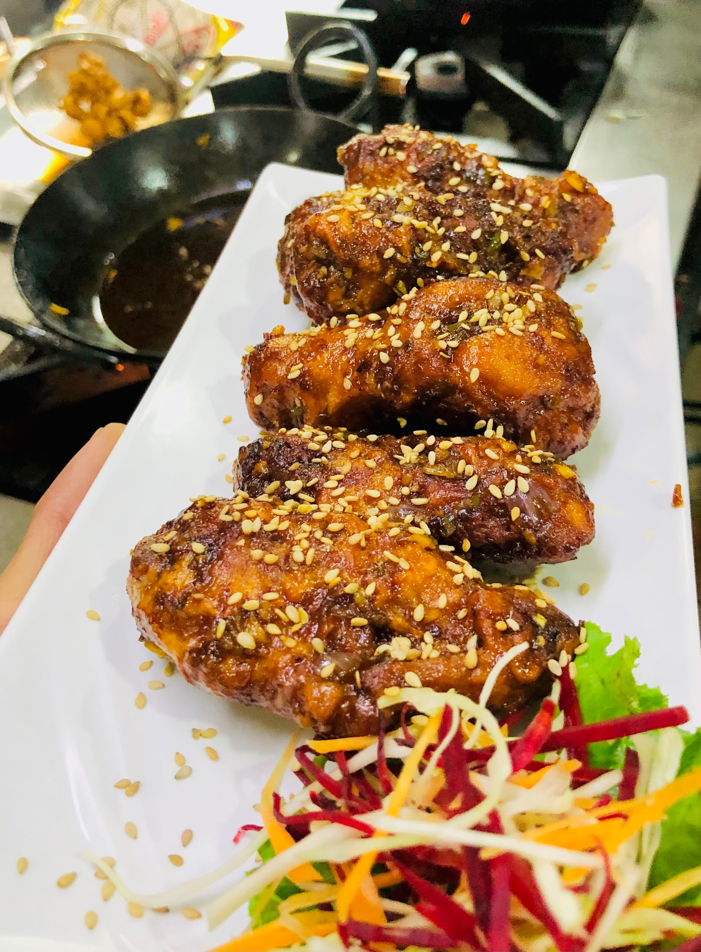 Glazed chicken wings sprinkled with sesame seeds on a white platter with fresh salad