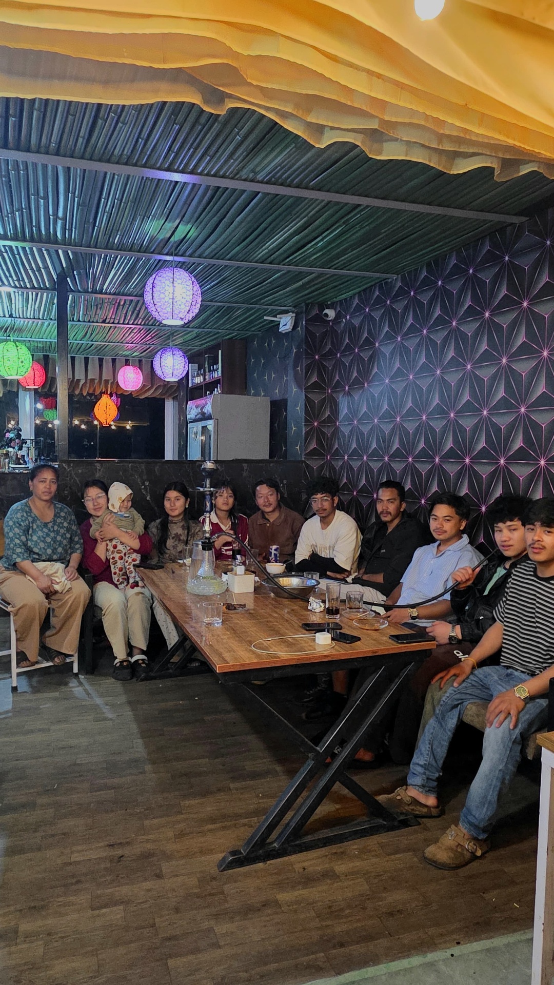 A large group seated around the long wooden table in the indoor lounge with hookah and patterned wall